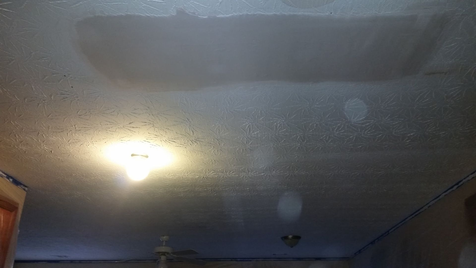 Water-stained ceiling with a dark, rectangular patch. A light fixture is visible below, casting light.