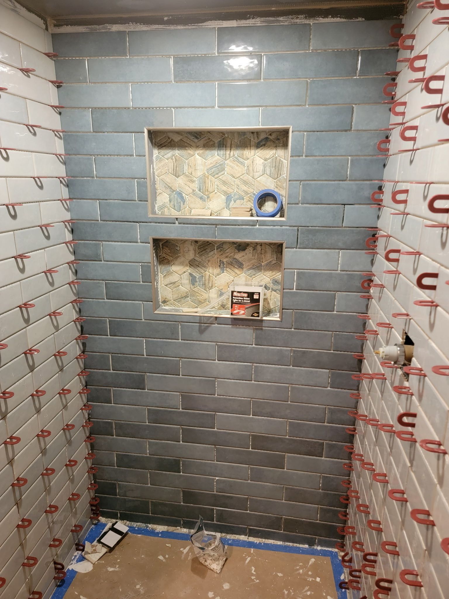 Bathroom shower with blue and white tiles in progress, with two tiled niches.