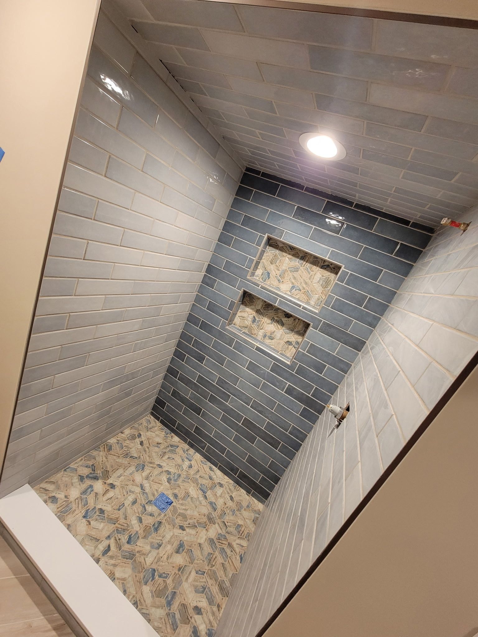 A tiled shower interior with blue-gray walls, a pebbled floor, and two built-in shelf niches.
