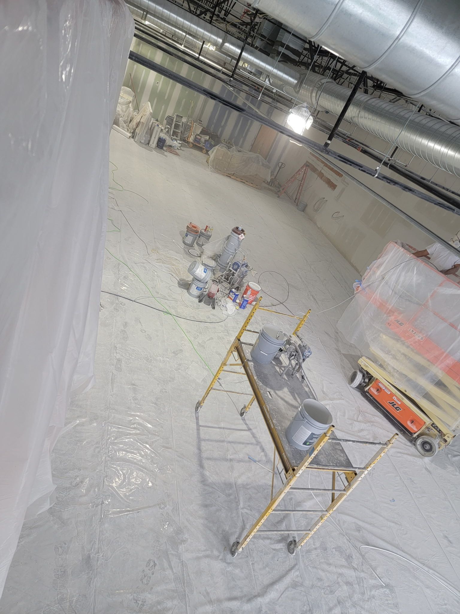 Large room with plastic sheeting, scaffolding, and assorted objects on the floor.