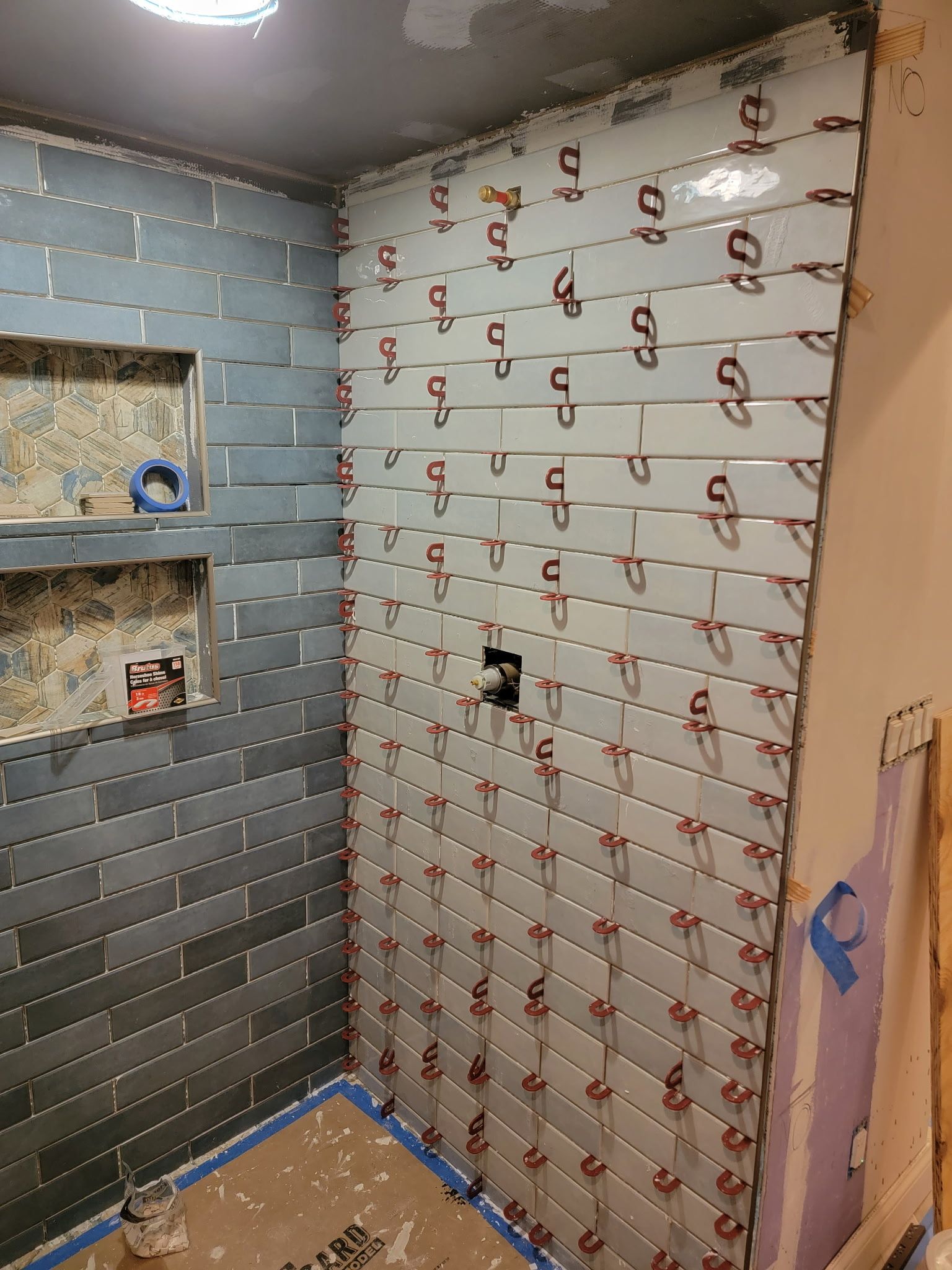 Bathroom under construction with blue and gray tiles and leveling clips.