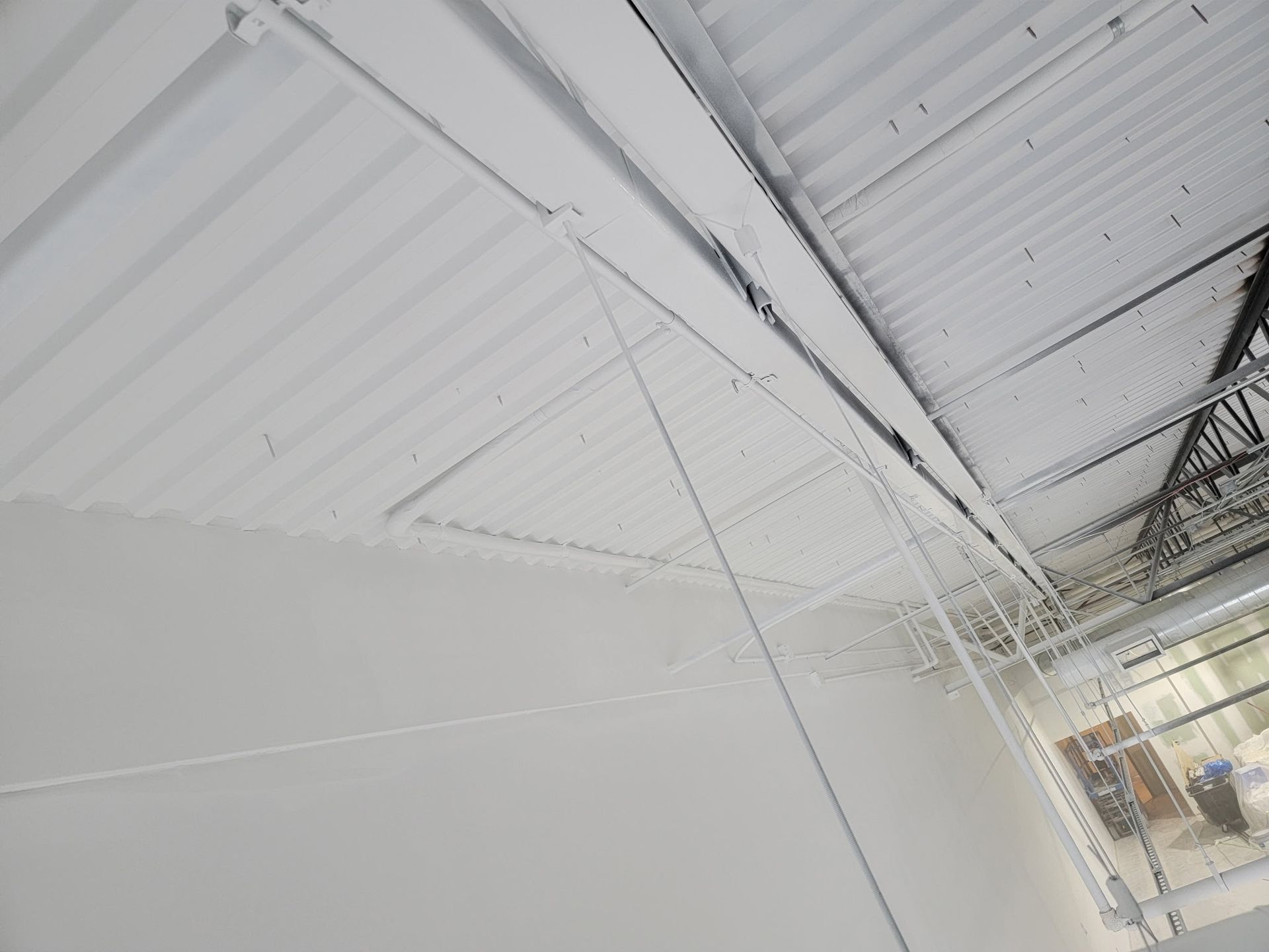 White ceiling and wall of a building. Corrugated metal roofing and beams.