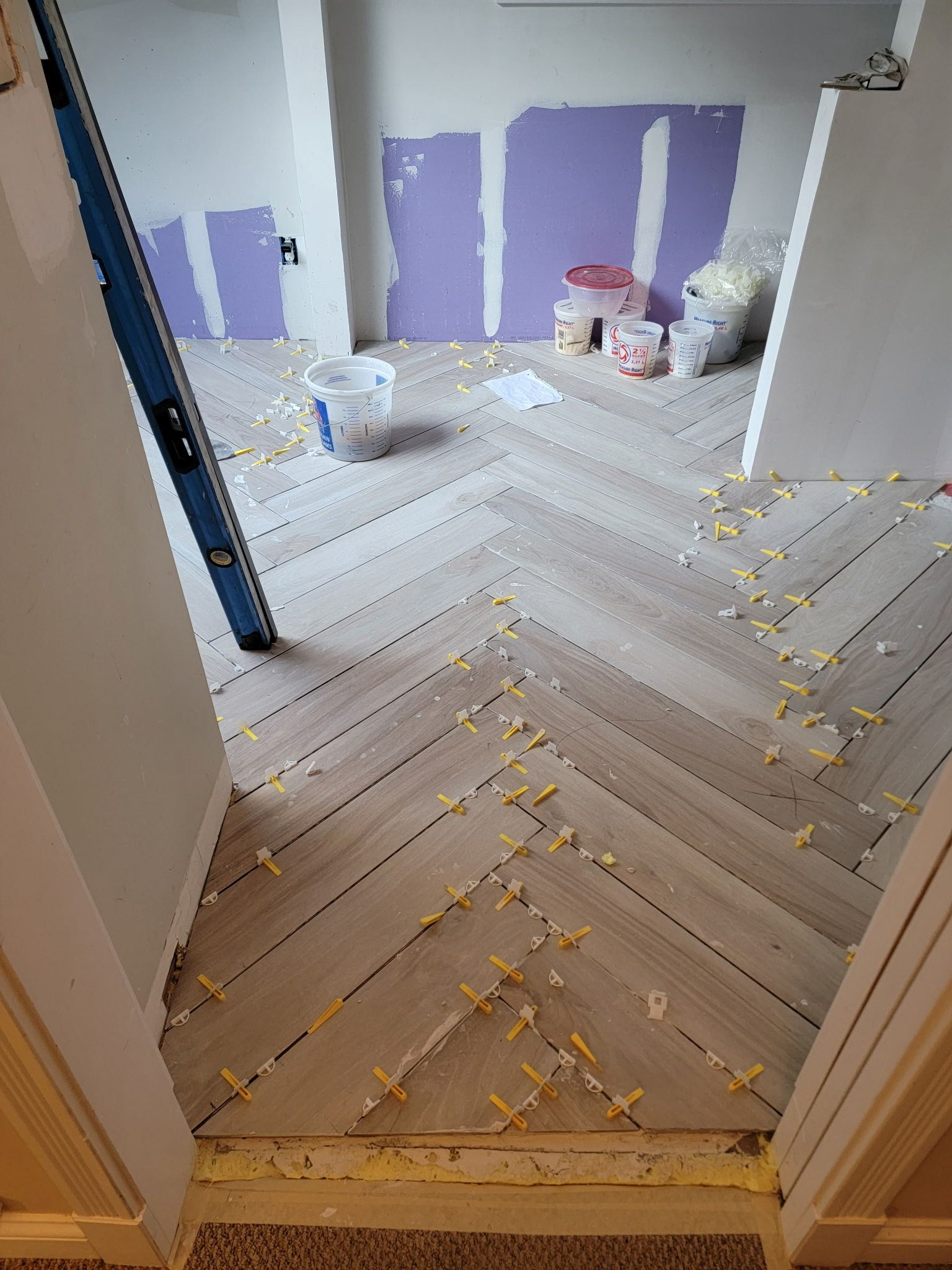 Herringbone tile floor installation in a room, with construction materials visible in the background.