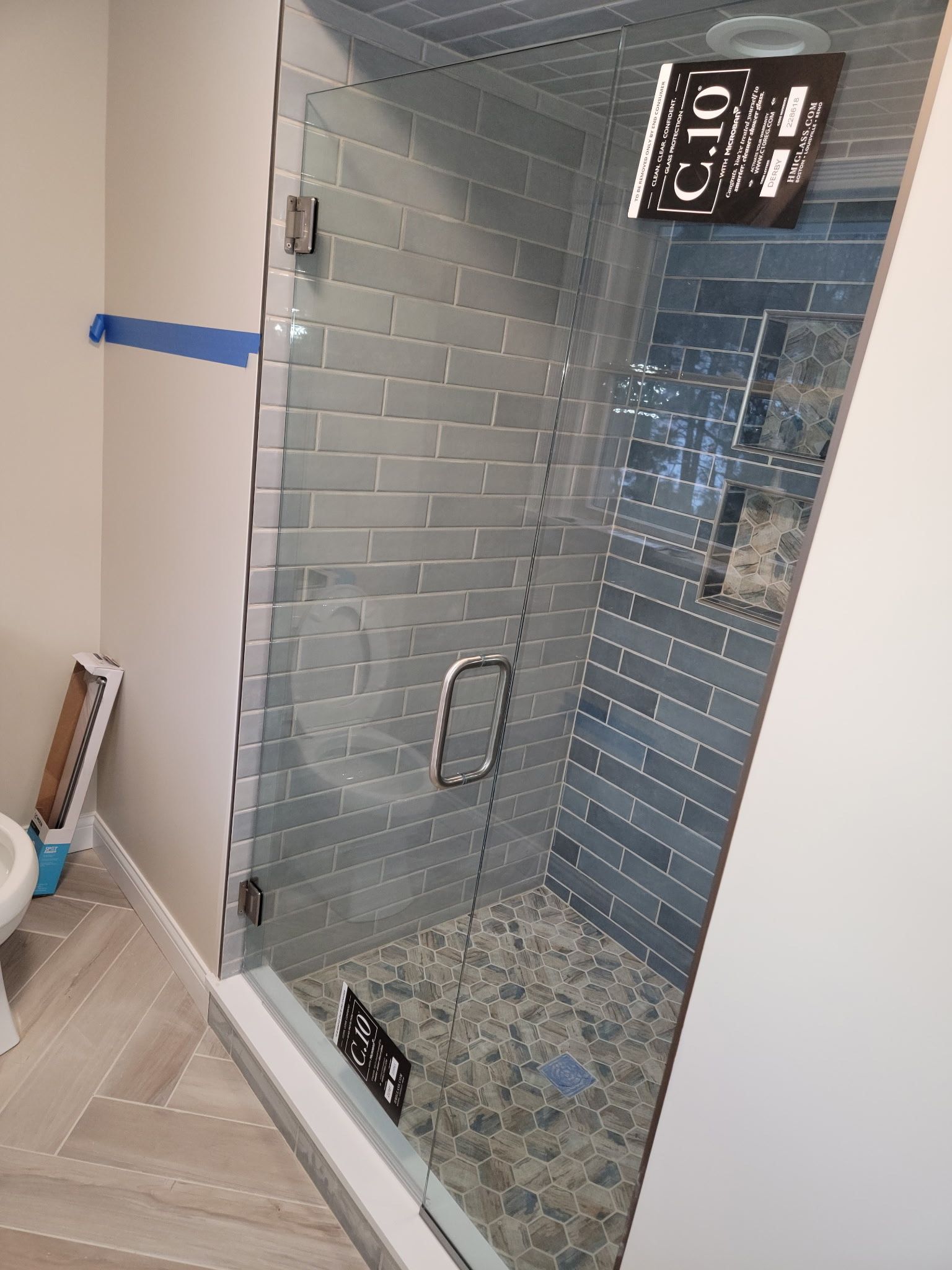 Glass-enclosed shower with blue tile walls and pebble floor. Silver door handle, fixtures, and hinges.