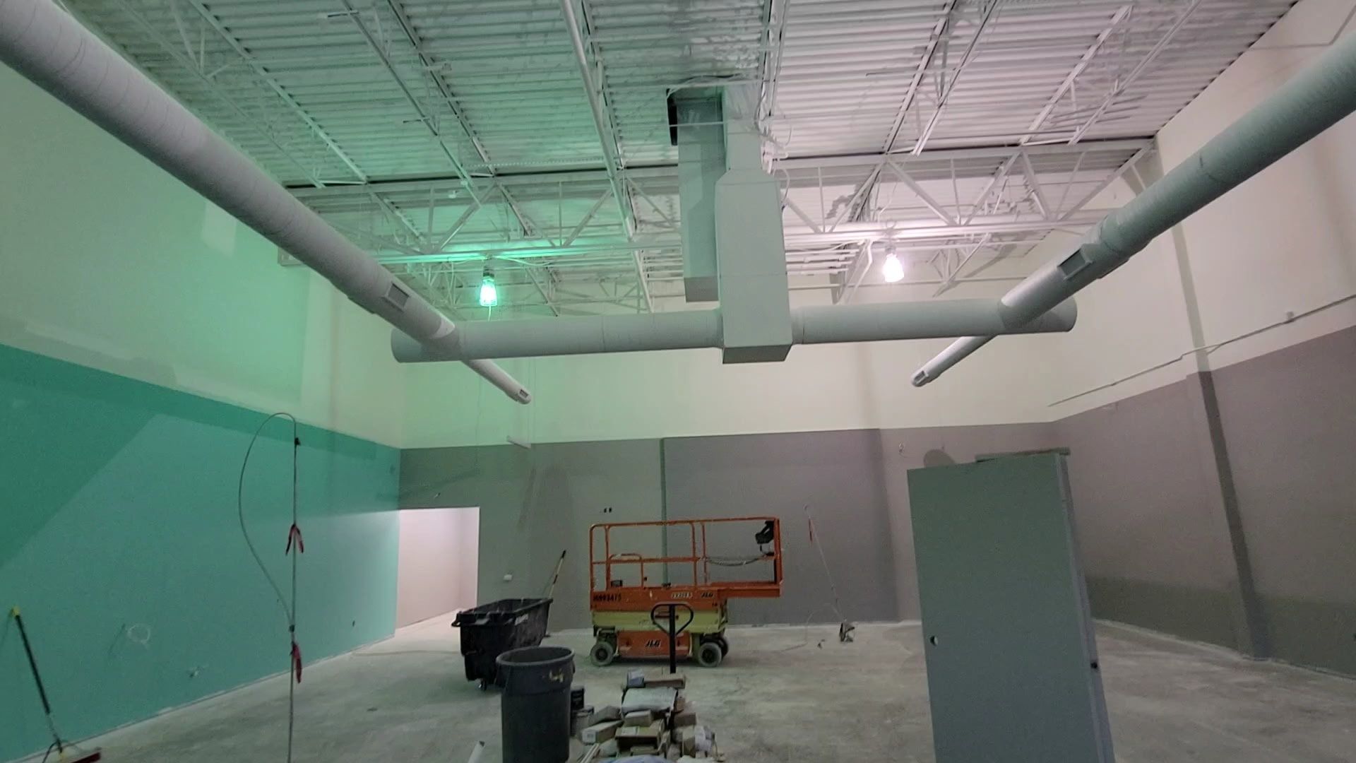 Interior of a building under construction, with gray and green walls, and overhead ventilation pipes.