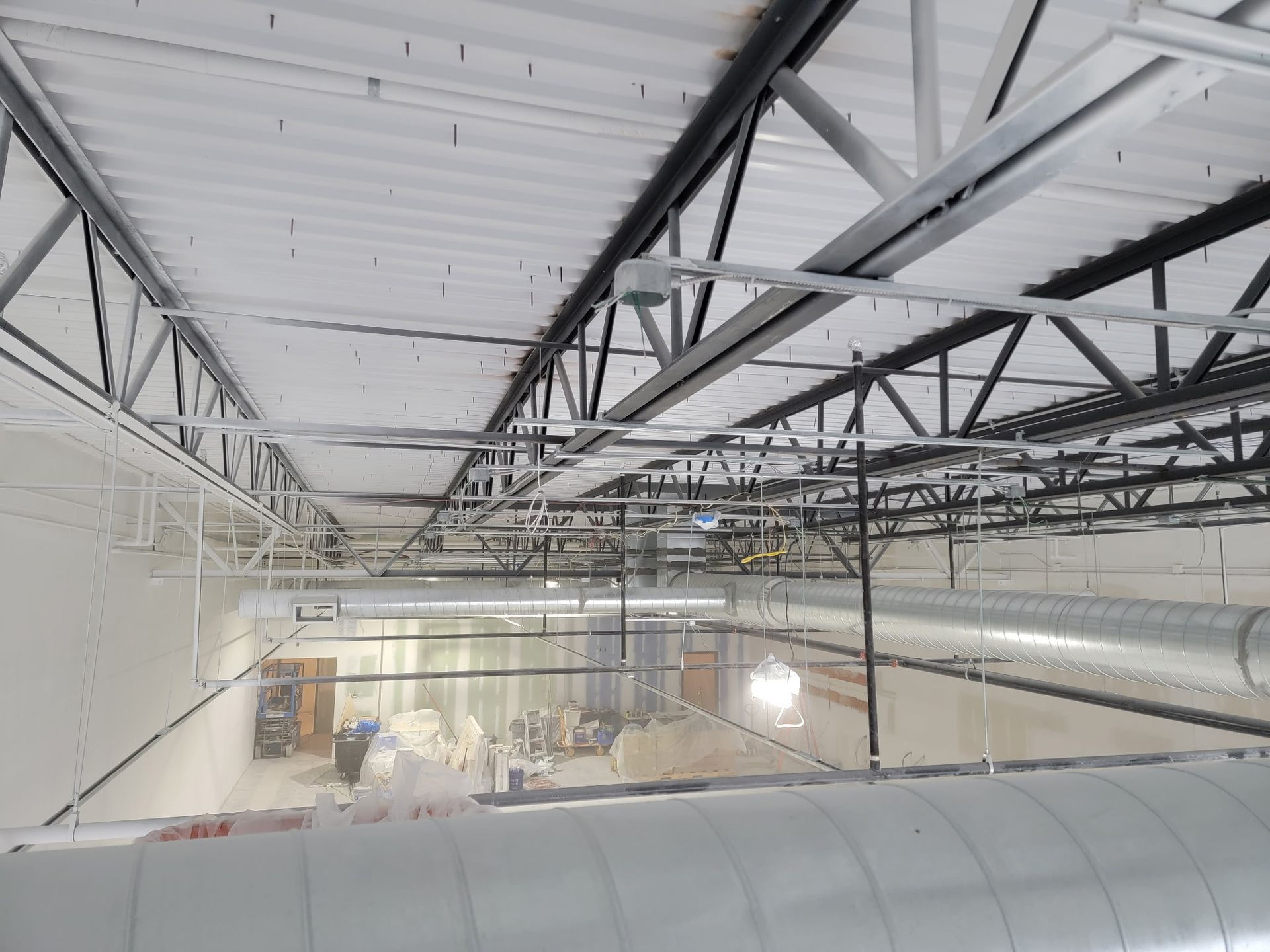 Interior view of a building under construction. White ceiling, metal beams, HVAC ducts, and exposed wiring.