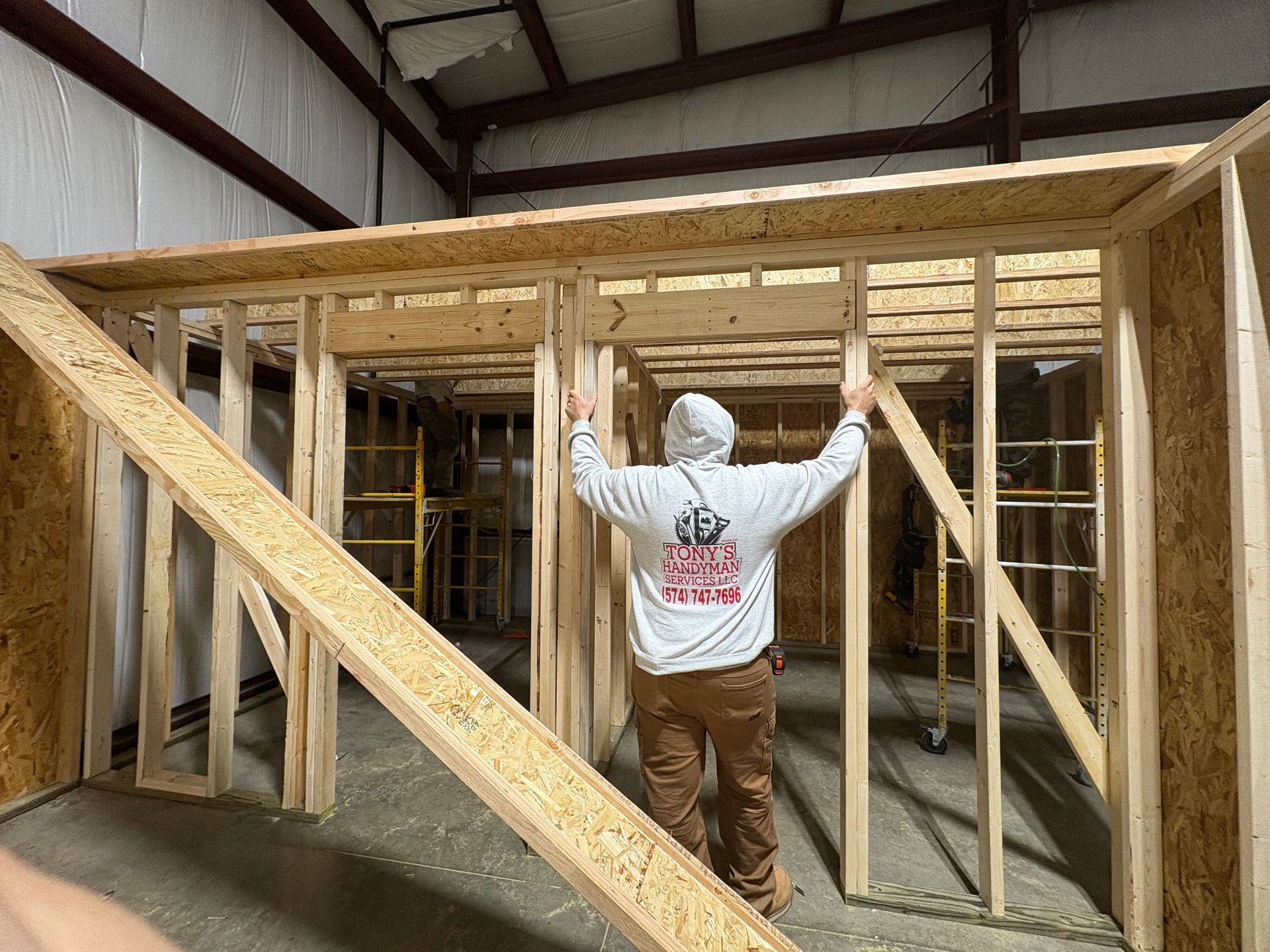Person in hoodie building wooden frame inside warehouse.