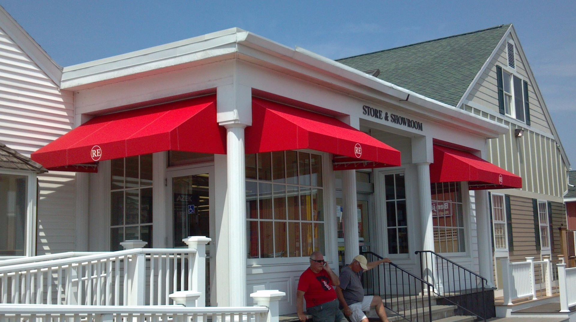 A man sits on the porch of a building with red awnings
