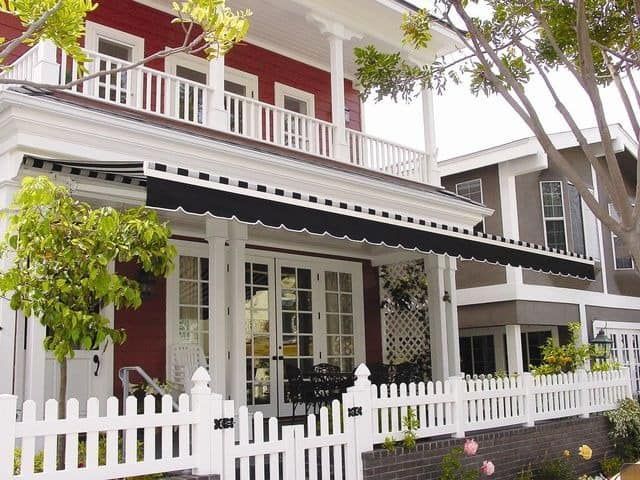 A red house with a black awning and a white picket fence