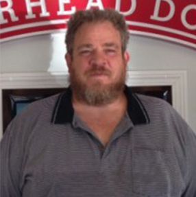 A man with a beard is standing in front of a sign that says rhead do