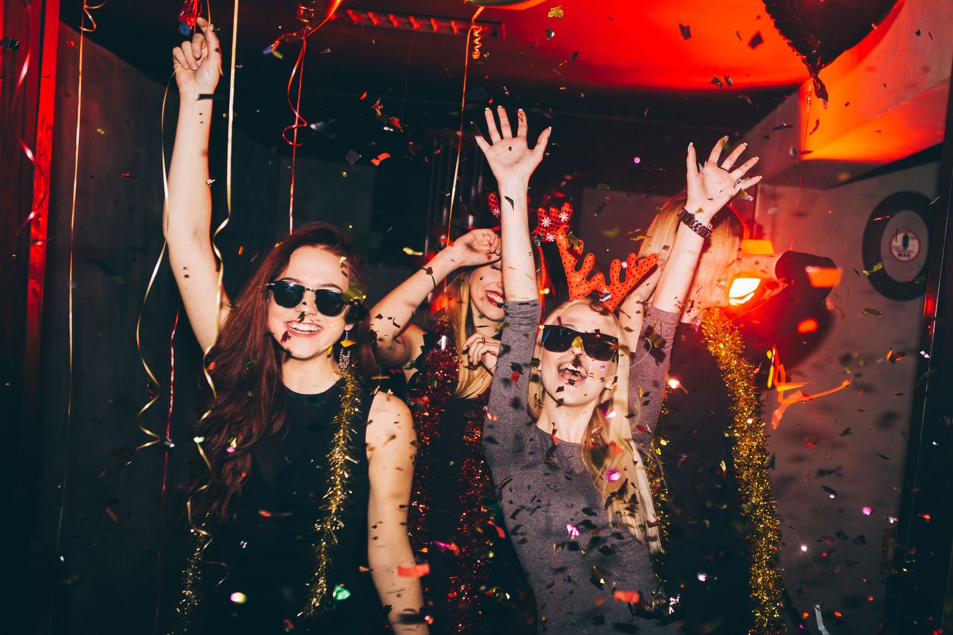 Two women are standing next to each other at a party with their arms in the air.