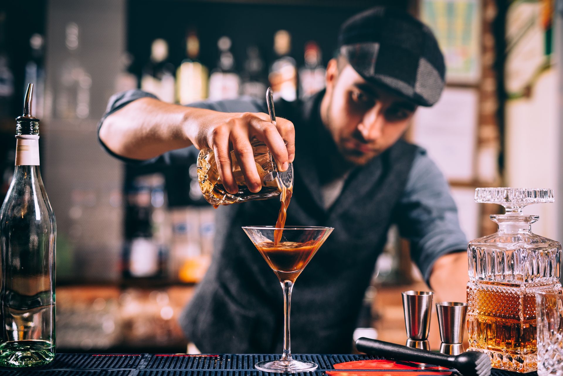 A bartender is pouring a drink into a martini glass.