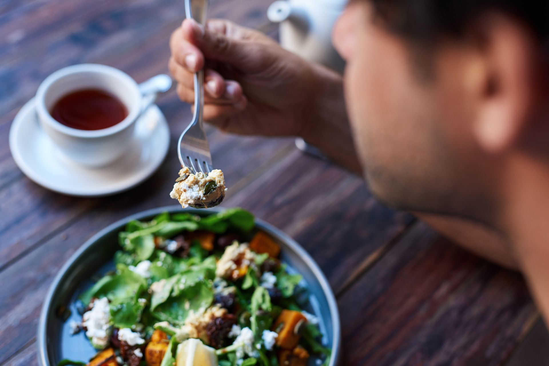 A man is sitting at a table eating a salad with a fork.