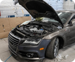 A dark gray Audi with its hood open in a workshop setting, undergoing repair | Firos Auto House 2