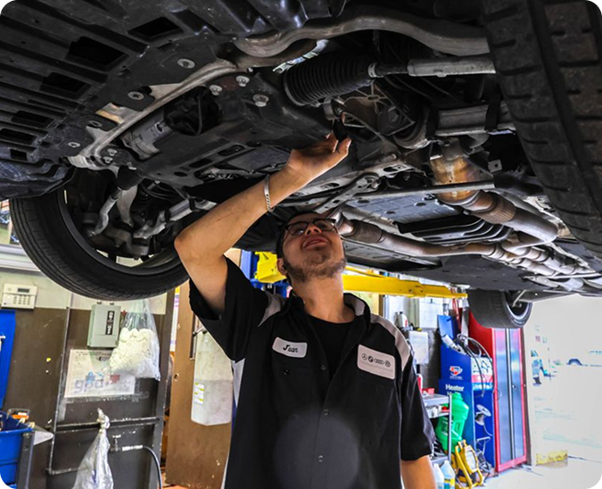 A mechanic works on the underside of a car hoisted on a lift in an automotive repair shop | Firos Auto House 2