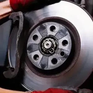 A mechanic wearing red gloves installs or inspects a metal car brake disc on a vehicle assembly.