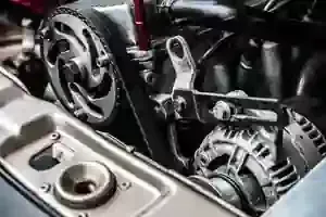 Close-up of a vehicle engine showing the alternator, a toothed pulley, and a drive belt under the hood.