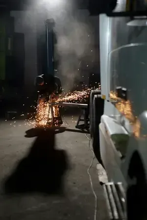 A worker grinds metal in a garage, creating a shower of sparks next to a parked semi-truck.