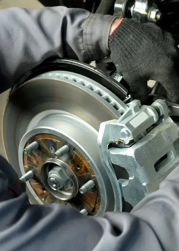 A mechanic wearing black gloves works on the disc brake assembly of a vehicle.