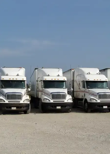 A mechanic with a beard leans over the open hood of a truck, working on the engine components in a garage setting.
