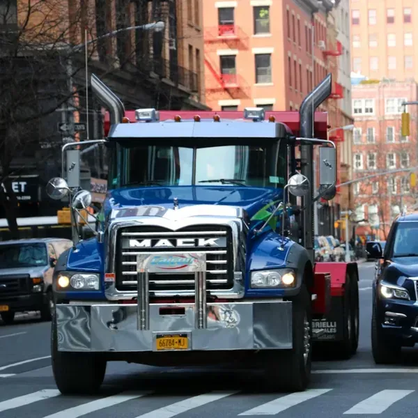 A blue Mack dump truck driving on a city street between other vehicles.