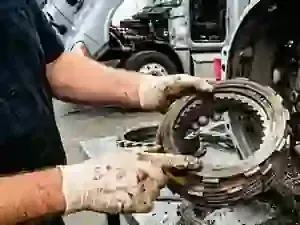 A mechanic wearing gloves holds and inspects a multi-plate clutch assembly in a vehicle repair shop.