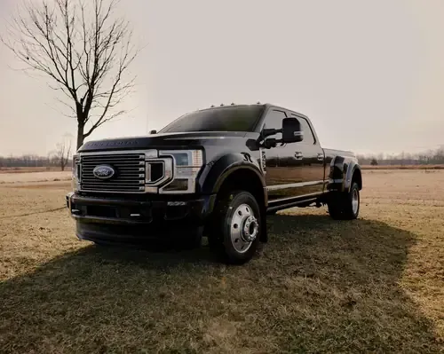 A black Ford Super Duty dually pickup truck parked on a field with a bare tree in the background.