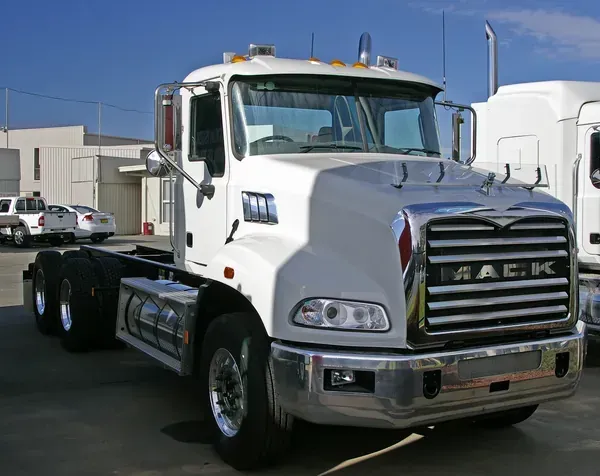 A white Mack semi-truck parked in an outdoor lot on a sunny day.