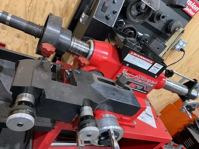 A red brake lathe machine with a cutting tool assembly mounted on its bed in a garage setting.