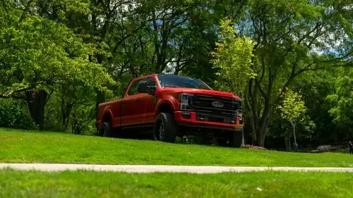A bright orange Ford Super Duty pickup truck parked on a grassy hill surrounded by trees.