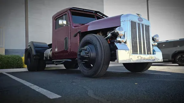 A custom maroon Peterbilt semi-truck with a chopped roof parked in an outdoor lot.