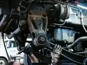 A mechanic wearing gloves works on the underside of a heavy-duty truck, inspecting or repairing the suspension system.