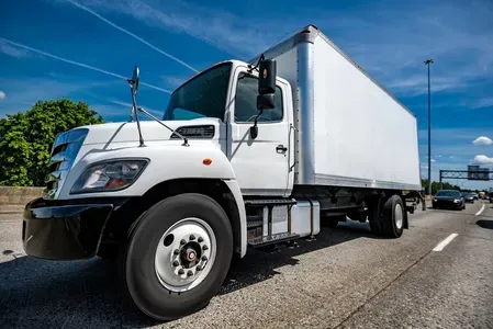 A white box truck driving on a multi-lane highway under a clear blue sky.