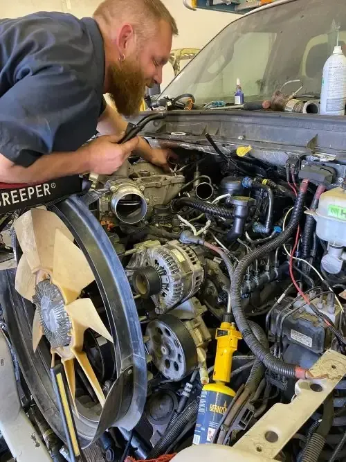 A mechanic leaning into the engine bay of a truck, performing maintenance on its exposed engine components.