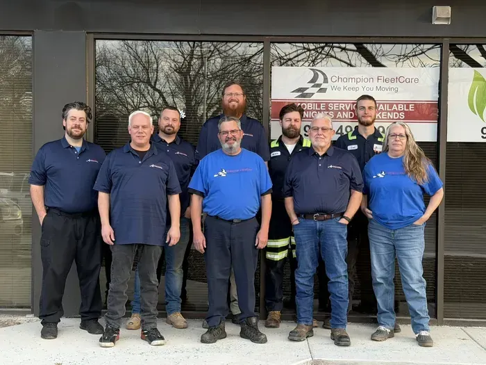 A group of employees in blue company shirts pose together in front of a Champion Fleet Care business window.