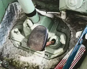 A close-up of a textured brake pedal next to a steering column on a light green, diamond-plate metal vehicle floor.
