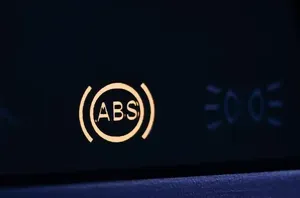 An illuminated yellow ABS warning light and a faint blue parking light symbol on a vehicle's dark dashboard.