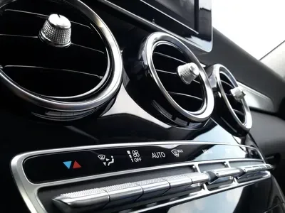 Close-up of circular car air vents and climate control buttons on a glossy black dashboard.