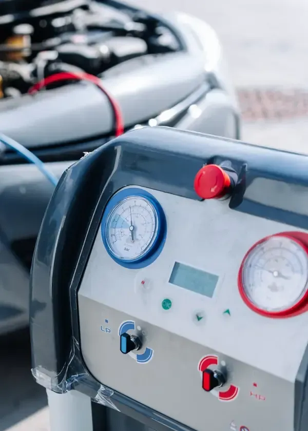 An AC service machine with pressure gauges and hoses connected to an open car engine bay.