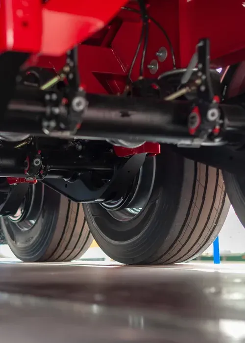 Close-up view of the underside of a red vehicle showing a black axle, suspension components, and tires on a light floor.