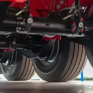 Close-up view of the underside of a red vehicle showing a black axle, suspension components, and tires on a light floor.