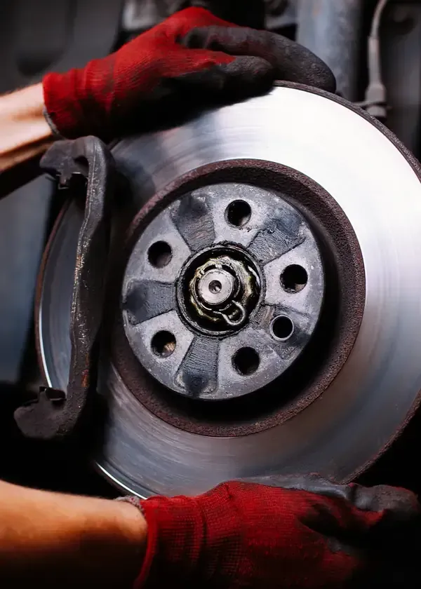 A mechanic wearing red gloves installs or inspects a metal car brake disc on a vehicle assembly.