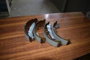 Four metal drum brake shoes for a vehicle, arranged on a wooden surface.