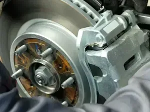A mechanic in work uniform and gloves repairing the brake system of a vehicle.