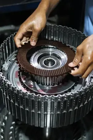 Hands assemble a metal transmission clutch disc into a gear housing in a mechanical workshop.