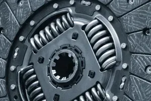 A close-up of a metal car clutch disc, showing its splined center hub, internal torsion springs, and friction material.