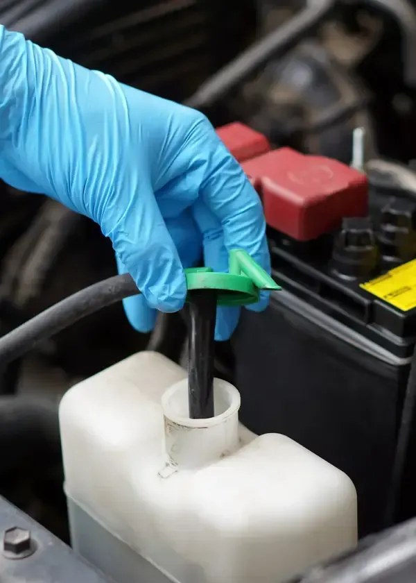 Gloved hand opening the green cap of a car's translucent fluid reservoir under the hood.