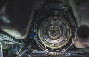 A close-up view of an automobile's engine flywheel and bell housing, showing the metal gear and mounting bolts.