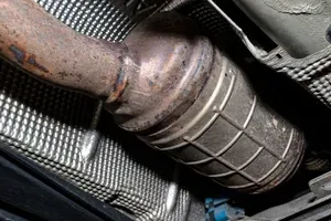 A metallic DPF is connected to an exhaust pipe, positioned above a textured silver heat shield.