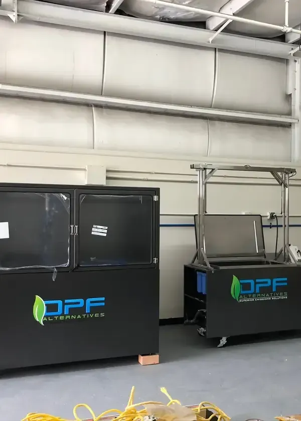 Two black DPF Alternatives cleaning machines for vehicle filters stand in an industrial indoor workspace.